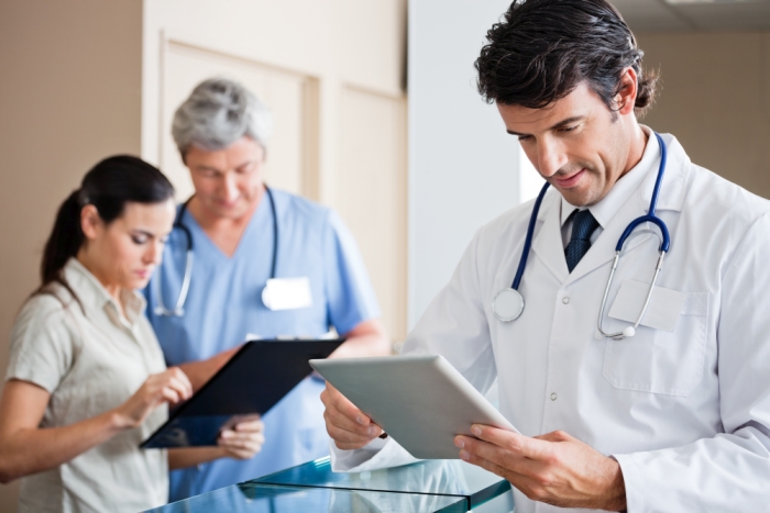 Mid adult male doctor holding digital tablet with colleague and receptionist standing in background