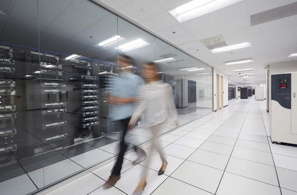 Male and female office workers walking together along the glass wall of an enclosed server room featuring open server racks, within a larger data center of Dell server products.