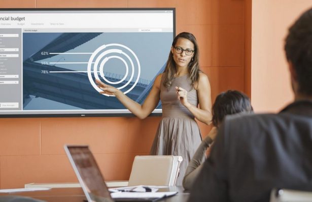 Businesswoman presenting a financial budget chart to colleagues in a conference room on a Dell 70 (Model C7016H) 70-inch conference room monitor