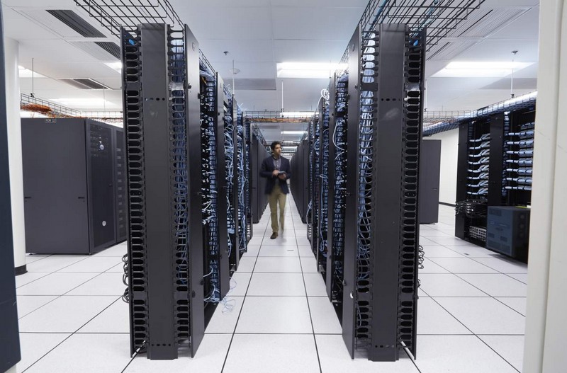 Male office worker walking between two rows of Dell server racks in a large data center, holding a Dell Venue 8 Pro 3000 Series (Model 3845, Bailey) tablet.